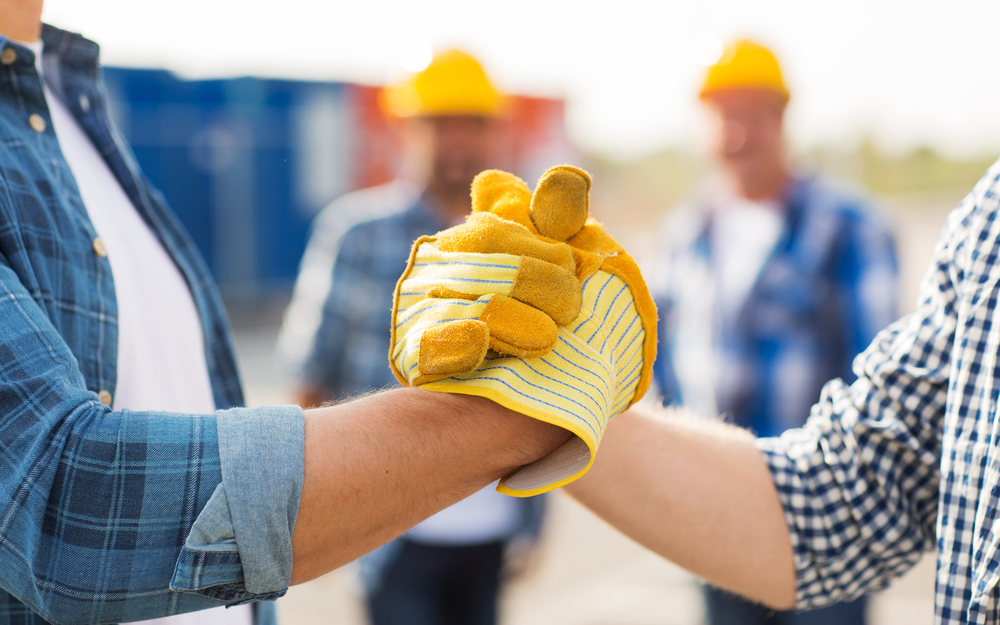 Two workers in hard hats clasping hands